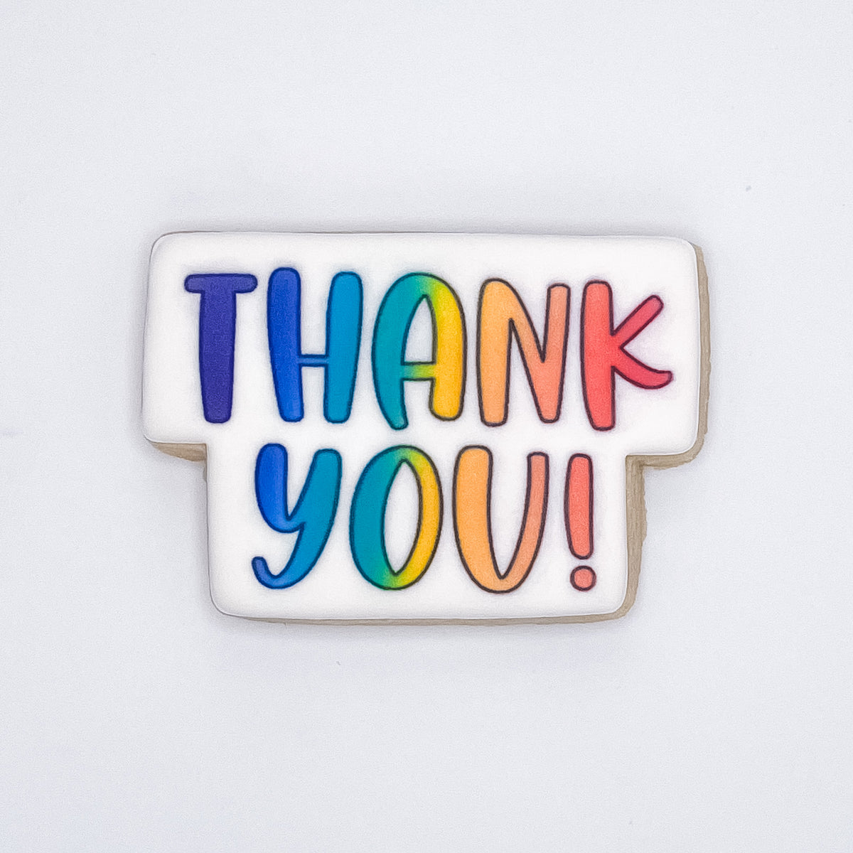 A square white-frosted cookie with the words 'THANK YOU!' written in large, colorful rainbow letters, shown on a plain white background.