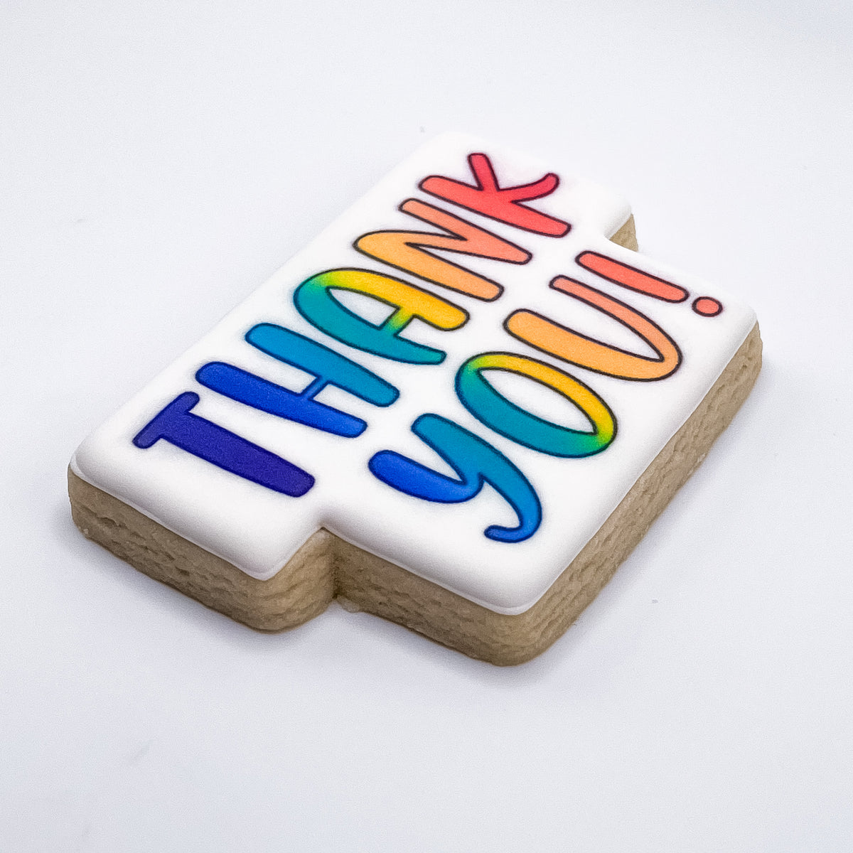 A rectangular sugar cookie with white icing and the words 'THANK YOU!' in large, colorful rainbow letters, photographed on a clean white background.
