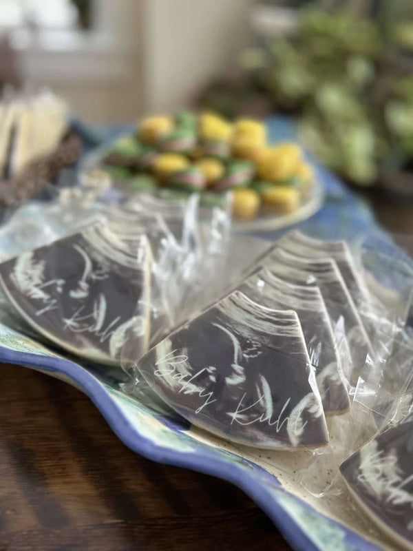 A close-up of packaged triangular chocolate pieces on a blue patterned tray, with a blurred plate of colorful candies in the background.